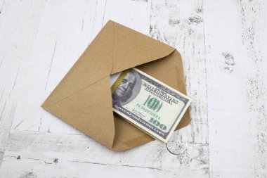 A brown envelope with a bundle of 100 dollars lies on a white wooden table
