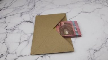 Eldivenli bir el, içinde banknotlar olan bir zarfın üzerine 10 avroluk banknotlar koyar.