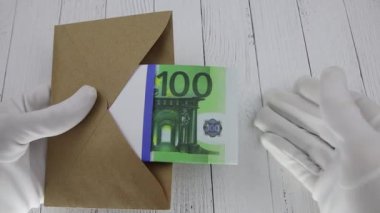 Beyaz bir eldiven, kahverengi bir zarfın içinde 100 Euro 'luk banknotları sayar.