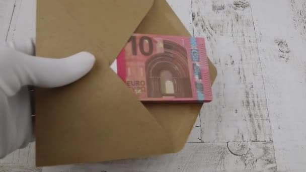 La main dans un gant blanc met une enveloppe avec un paquet de 10 billets d'euros sur une table — Video