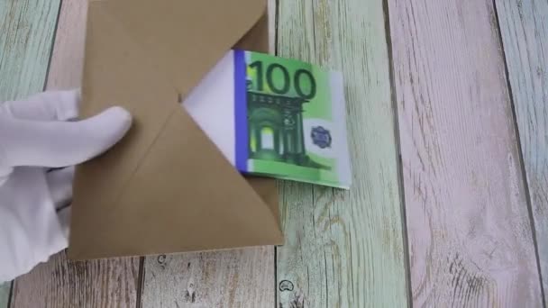 Ręka w białej rękawicy kładzie kopertę z paczką banknotów 100 euro na stole — Wideo stockowe