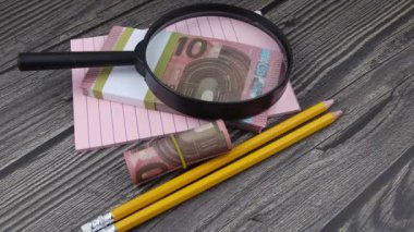 Ofis malzemeleriyle dolu 10 avroluk banknotların üzerinde bir büyüteç duruyor..