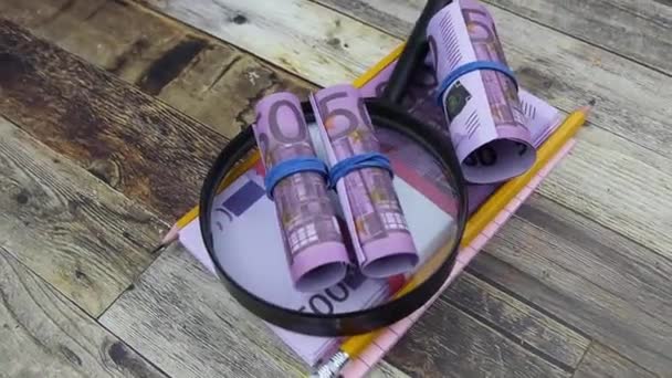 Una lente d'ingrandimento si trova su un pacchetto di 500 banconote in euro con forniture per ufficio. — Video Stock