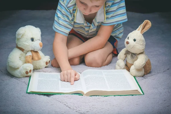 Kleine jongen lezen boek met zijn favoriete speelgoed — Stockfoto