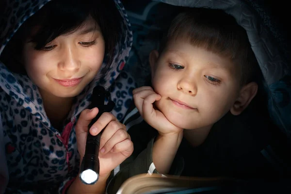 Children reading book under the covers