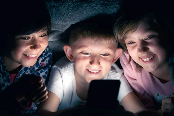 Children at night under the covers with smartphone