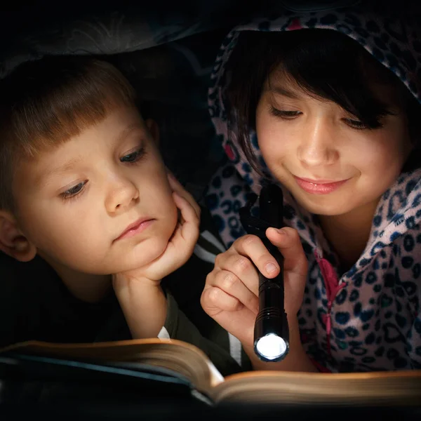 Çocuklar örtünün altında kitap okuyor.