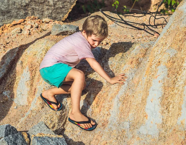 Anak laki-laki nakal hooligan lucu memanjat batu batu batu dalam flip flops. Pilih pakaian kaki untuk permainan olahraga alam. Peringatkan anak-anak tentang bahaya keselamatan di luar ruangan, kesulitan orang tua pendidikan, jagalah — Stok Foto