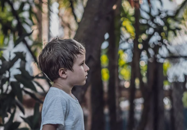Side view gyerek hat éves fiú néz egyenes komoly szomorú fehér póló kívül természet háttér. Sötét hangulat, gyermekkori szülői pszichológiai nevelési problémák válság a COVID koncepció miatt — Stock Fotó