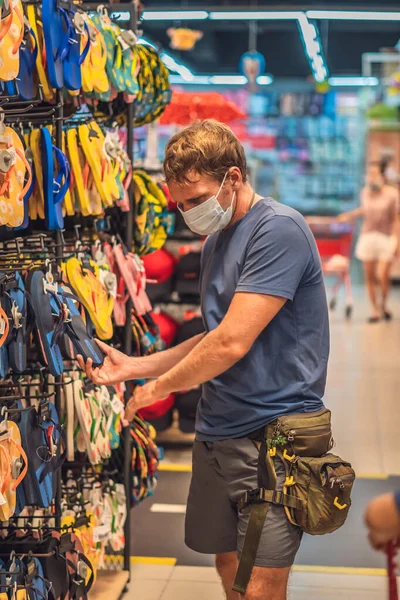 Pria serius biru dalam t-shirt biru memilih sepatu di toko, mengenakan topeng wajah biru melindungi dari virus COVID, ukuran kontrol kesehatan pribadi publik, belanja selama pandemi, membeli pakaian baru — Stok Foto