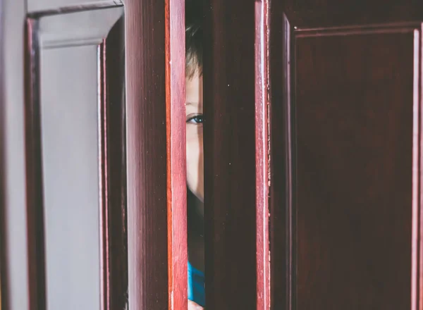 Anak laki-laki sedih bersembunyi di lemari, close-up melihat mata biru di pintu ajar celah lemari pakaian rumah. Emosi anak. Tanda gejala peringatan, perawatan untuk anak remaja penyakit depresi, ketakutan, kehidupan keluarga — Stok Foto