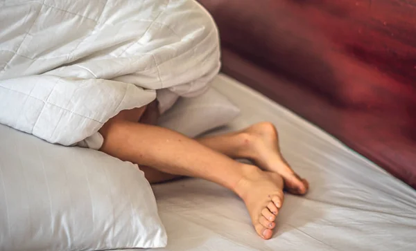Sisi close-up melihat kaki anak laki-laki lutut menonjol di bawah selimut putih di tempat tidur. Tidur dan bersantai konsep, kelembutan pagi mimpi bayi atau mimpi buruk, bermain bersembunyi, kulit nyata — Stok Foto