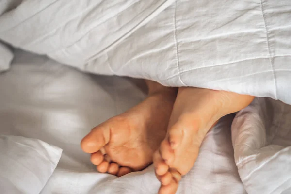Sisi dekat melihat anak laki-laki dua kaki menonjol bawah selimut putih di tempat tidur. Tidur dan bersantai konsep, kelembutan pagi mimpi bayi atau mimpi buruk, bermain bersembunyi, kulit nyata — Stok Foto