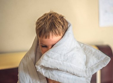 Ön cephede oturan beyaz çocuk beyaz saçlı çocuk yatak odasındaki beyaz battaniyeden fırlamış. Kaliteli uyku zamanı ya da uyan, rahatla, sabah şefkati, bebek rüyası ya da kabus, saklambaç oyna.