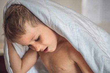 Yakın plan beyaz çocuk beyaz saçlı çocuk yatak odasındaki beyaz battaniyeden sarkıyor. Kaliteli uyku zamanı ya da uyan, rahatla, sabah şefkati, bebek rüyası ya da kabus, saklambaç oyna.