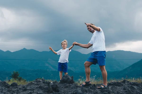 Father son or adult younger brother walk. Cloudy sky before rain, mountain background. Man show points finger into distance, serious boy look far away. Solve problems together. Natural education — Stock Photo, Image