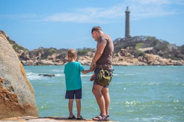 Babanın umrunda. Deniz kenarında oğlu var. Birlikte zaman geçirip yeni şeyler keşfediyoruz. Çocuk elini tutan adam. Deniz feneri arka planı bireysel bilincin sembolü, çocuk yetiştirme, baba aile birliği mutlu çocuk üzerindeki etkisi
