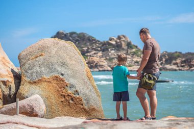 Babam Son 'ı deniz kenarında önemsiyor, birlikte zaman geçirip yeni şeyler keşfediyor. Çocuk elini tutan adam, aşağı baksın. Doğa kayası. Çocuk yetiştirmek, baba aile birliği mutlu çocuk nüfuzu, hafta sonu çocuklarla yaşamak.