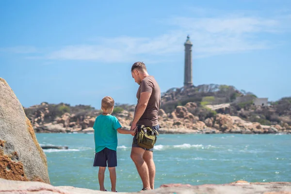 Dad care Son near sea, walk spend time together explore new. Man hold kid hand. Lighthouse background Symbol of individual consciousness, raising boy, father family union influence in happy child live