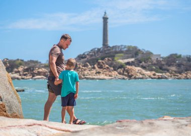 Babanın umrunda. Deniz kenarında oğlu var. Birlikte zaman geçirip yeni şeyler keşfediyoruz. Çocuk elini tutan adam. Deniz feneri arka planı bireysel bilincin sembolü, çocuk yetiştirme, baba aile birliği mutlu çocuk üzerindeki etkisi