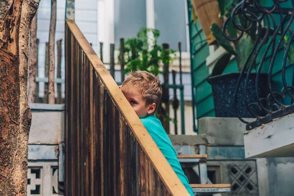 Copia Espacio estilo de vida divertido foto niño movimiento sentarse escaleras de madera fuera pasamanos, buscar la sonrisa expresión facial, jugar a las escondidas. Concepto nuevo juego de niños, educación, comportamiento, bienes para niños —  Fotos de Stock