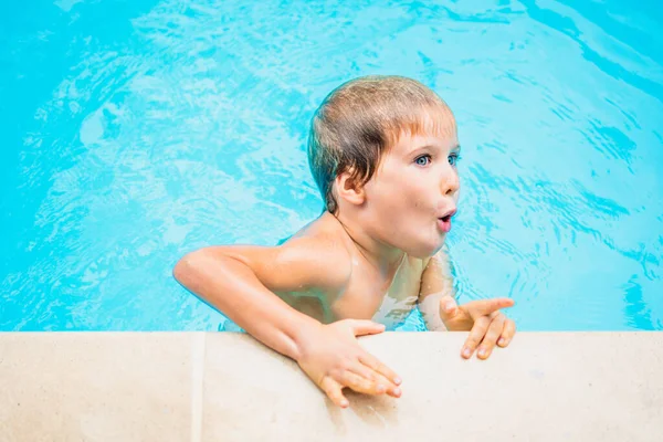 Gaya hidup anak laki-laki potret lucu berenang di kolam renang, memegang tepi, air biru cerah. Terkejut melihat bersemangat, jari menunjuk. Perilaku anak-anak, hiburan taman air, perkemahan musim panas, pelatihan kegiatan rekreasi — Stok Foto