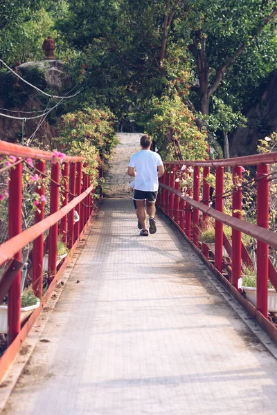 Pemandangan belakang Manusia melintasi jembatan gantung besi merah menuju taman hutan. Olahraga Outdoor setelah karantina, jelajahi kehidupan baru — Stok Foto
