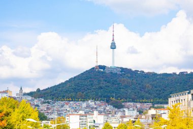 Namsan Seul Kulesi 'nin 25 Ekim 2025' te Güney Kore, Seul 'deki bir tepe ve şehir binasının üzerinde sonbahar renkleriyle ve gökyüzünde parlak bulutlarla çekilmiş görüntüsü.