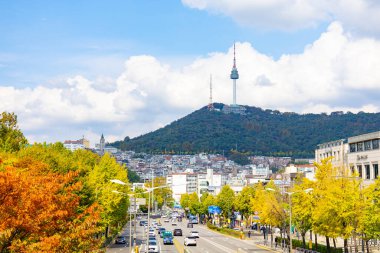 Renkli sonbahar ağaçları ve Güney Kore 'deki Namsan Seul Kulesi' nin bulunduğu işlek bir caddede 25 Ekim 2025 'te parlak bulutlar ve mavi gökyüzü altında yakalanan araçların yayın görüntüsü.