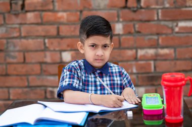 Küçük şirin Hintli / Asyalı okul çocuğu çalışma masasında çalışıyor, kalemle deftere yazıyor..