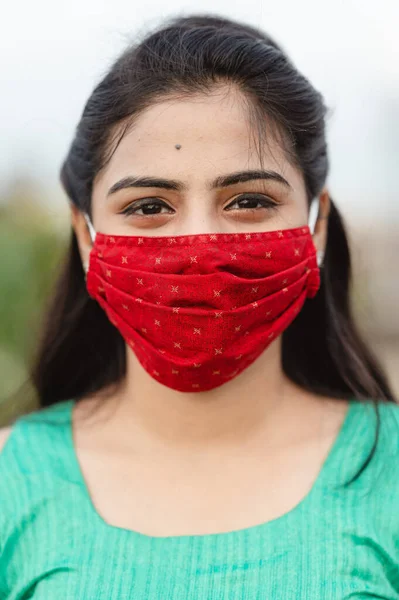 Beautiful smiling Indian young woman in protective face mask, happy millennial female in medical facial cover from COVID-19 , healthcare concept, isolated over outdoor background