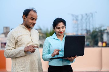 İnternette orta yaşlı bir adama bilgisayar ve teknoloji öğreten resmi giysili genç Hintli bir kadın..