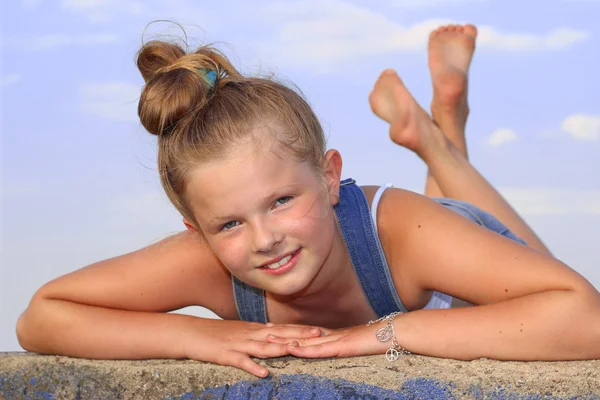 Cheerful little girl lying on her stomach on the wall — Stock Photo, Image