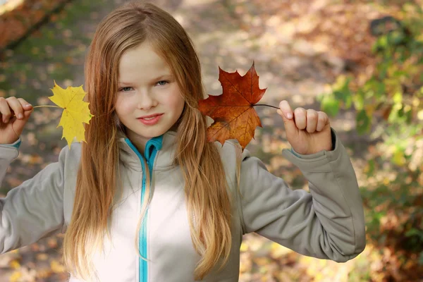 Mädchen spaziert zu zweit und hält zwei Herbstblätter in der Hand — Stockfoto
