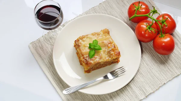 Lasagne on white plate with basi, fresh tomatoes and red wine — Stock Photo, Image