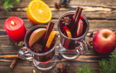 Tarçınlı sıcak şarap, yıldız anason ve ahşap bir masada meyve ile süslenmiş birkaç cam bardak. Geleneksel sıcak kış içeceği kavramı.