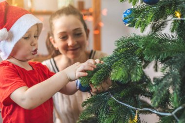 Anne ve küçük oğlu Noel ağacını oyuncaklar ve Noel toplarıyla süslüyorlar. Yeni yıl arifesinde evde mutlu aile zamanları.
