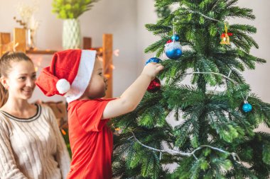 Anne ve küçük oğlu Noel ağacını oyuncaklar ve Noel toplarıyla süslüyorlar. Yeni yıl arifesinde evde mutlu aile zamanları.