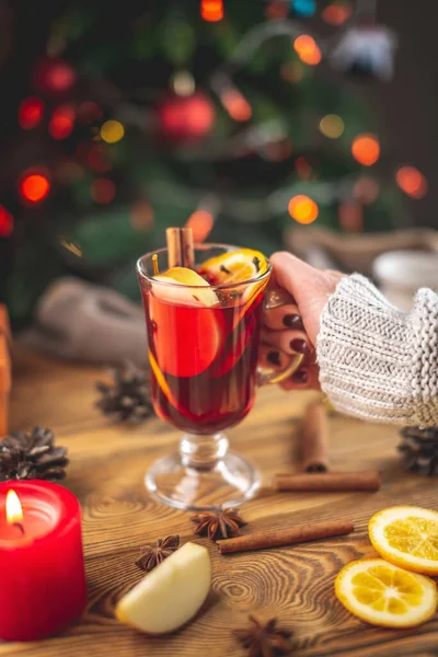 暖かいセーターに身を包んだ女性の手には クリスマスツリーを背景にライト付きの香り高いホット ホット マルチ ワインが注がれています お祝いの雰囲気のコンセプト — ストック写真