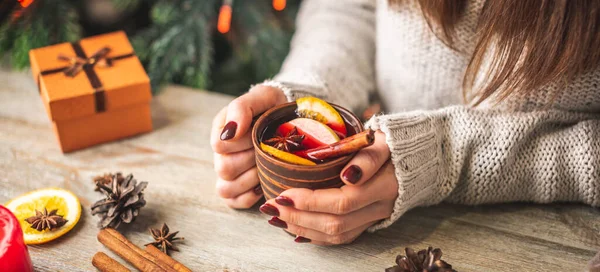 暖かいセーターの女性の手は 木製のテーブルの上に芳香族ホットマルチワインのカップを保持しています お祝いの雰囲気と居心地の良い冬の気分の概念 — ストック写真