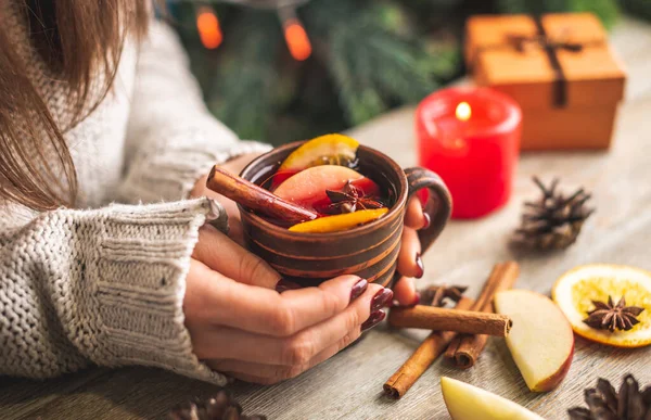 暖かいセーターの女性の手は 木製のテーブルの上に芳香族ホットマルチワインのカップを保持しています お祝いの雰囲気と居心地の良い冬の気分の概念 — ストック写真