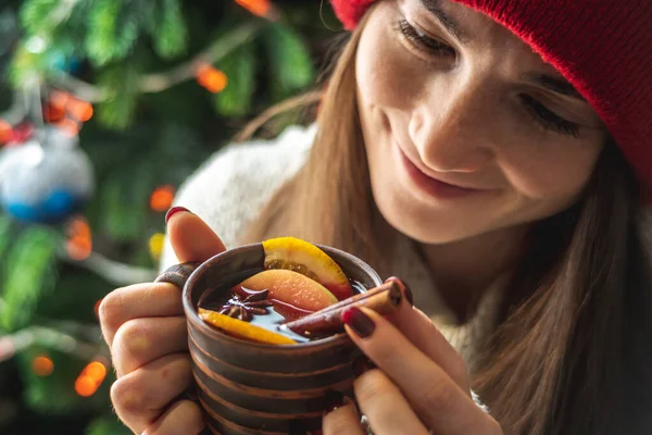 暖かいセーターに身を包んだ女性は クリスマスツリーを背景にライト付きの香り高いホット ホット ミュール ワインを持っています 休日の雰囲気と居心地の良い冬の気分の概念 — ストック写真