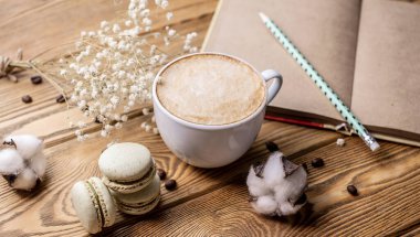 Bir fincan aromatik kahve, kurabiyeler ve ahşap bir masanın üzerinde bir defter. Kahve molası ve yaşam tarzı kavramı