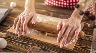 Kadın, mutfakta lezzetli ev yapımı kurabiyeler yapmak için ahşap bir masaya çiğ hamur atıyor..