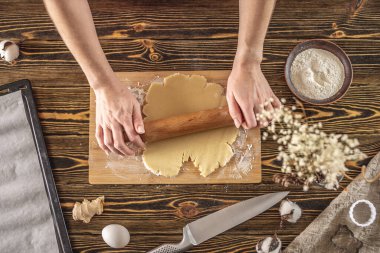 Kadın, mutfakta lezzetli ev yapımı kurabiyeler yapmak için ahşap bir masaya çiğ hamur atıyor..