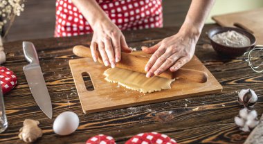 Kadın, mutfakta lezzetli ev yapımı kurabiyeler yapmak için ahşap bir masaya çiğ hamur atıyor..