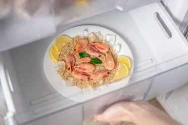 Kadın elleri buzdolabından bir tabak pirinç, karides ve limon çıkarıyor. Dondurulmuş yemek yapma ve yemek pişirme kavramı..