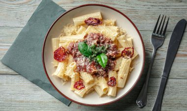 Tahta bir masada domates soslu, domatesli, peynirli ve fesleğenli lezzetli vejetaryen makarna tabağı. Üst görünüm.