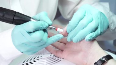 Usta, bir tırnak matkabıyla müşterilerin tırnaklarındaki jel cilasını çıkarıyor. Profesyonel manikür yapma süreci kavramı