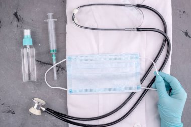 Beyaz tıbbi önlük, şırınga, steteskop, maske ve eldiven. Gri arka planda doktor için araç gereç ve koruyucu ekipman.